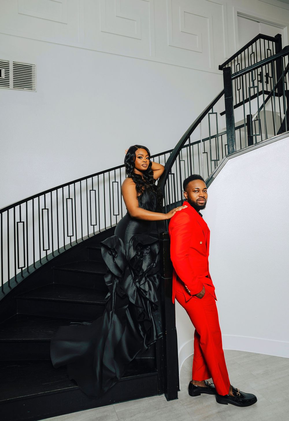 Fashion photoshoot featuring dramatic contrast between black and red outfits against a minimalist white interior setting.