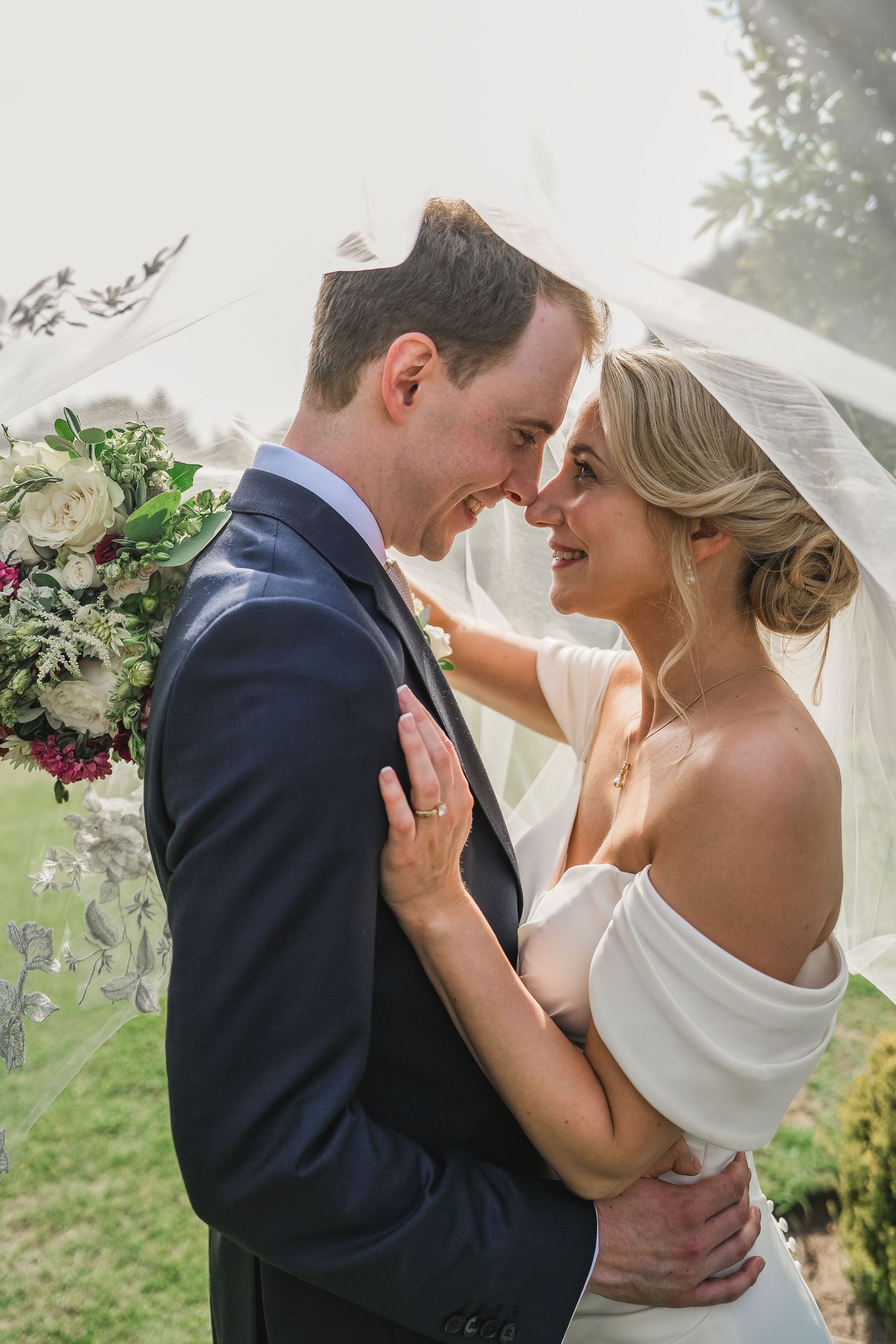 A beautifully caught, intimate moment for this handsome couple. The bride has her hair in a low, curled chignon bun. Soft, dewy makeup.