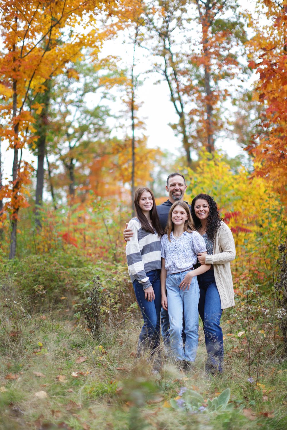 A group enjoys a casual outdoor photo session among vibrant autumn foliage and tall trees.