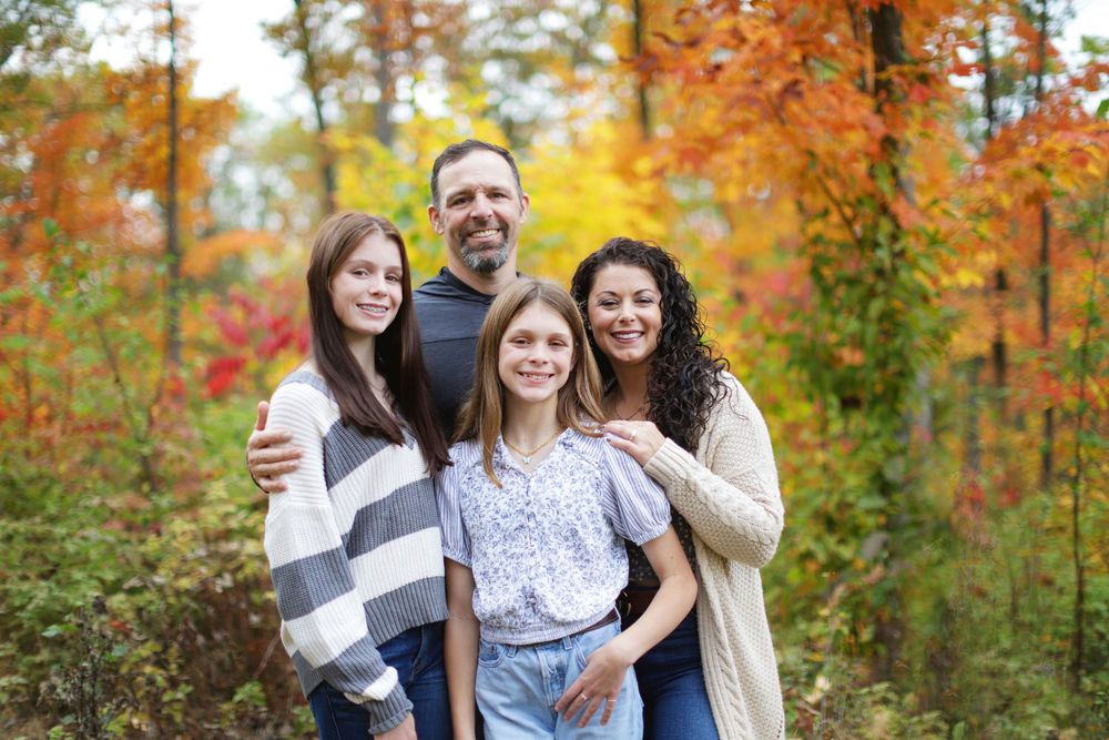 Family enjoying a fall photoshoot together outdoors surrounded by vibrant orange autumn foliage.