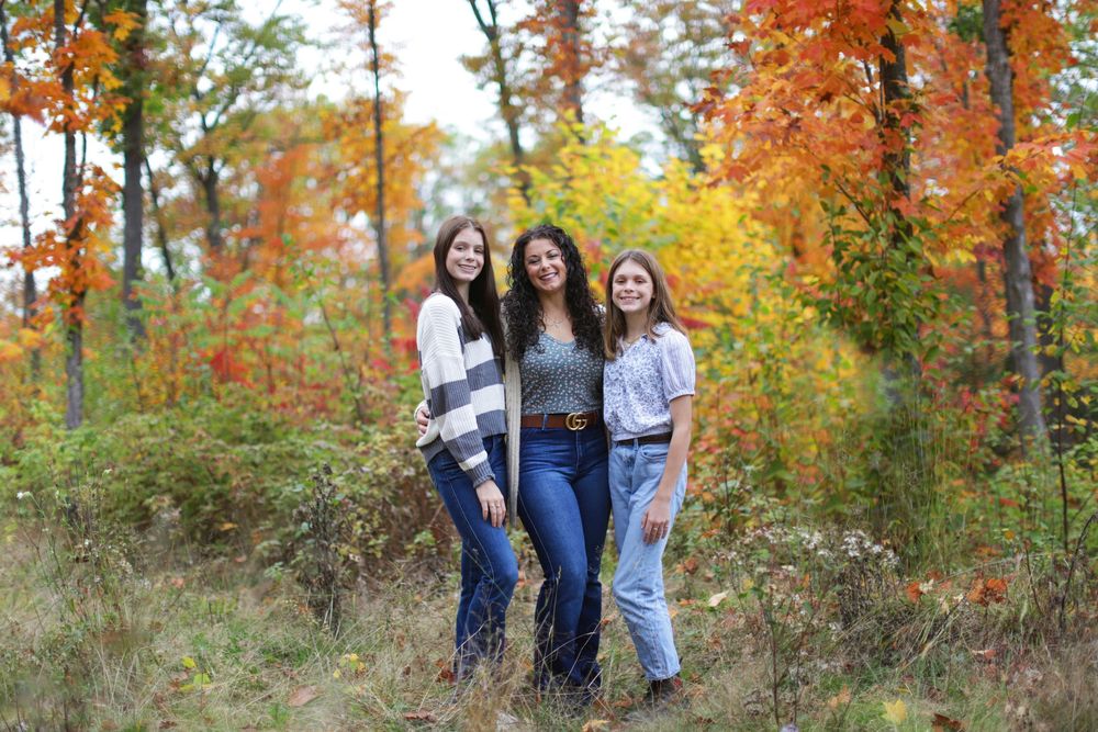 Group enjoying a fall photoshoot among vibrant autumn foliage and trees in a natural outdoor setting.