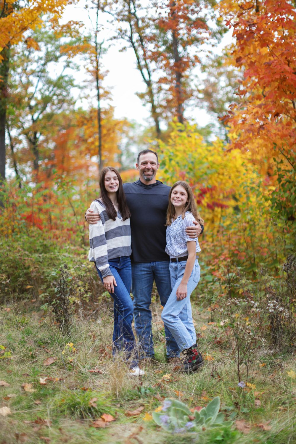 A group poses together against vibrant fall foliage in a natural outdoor setting.