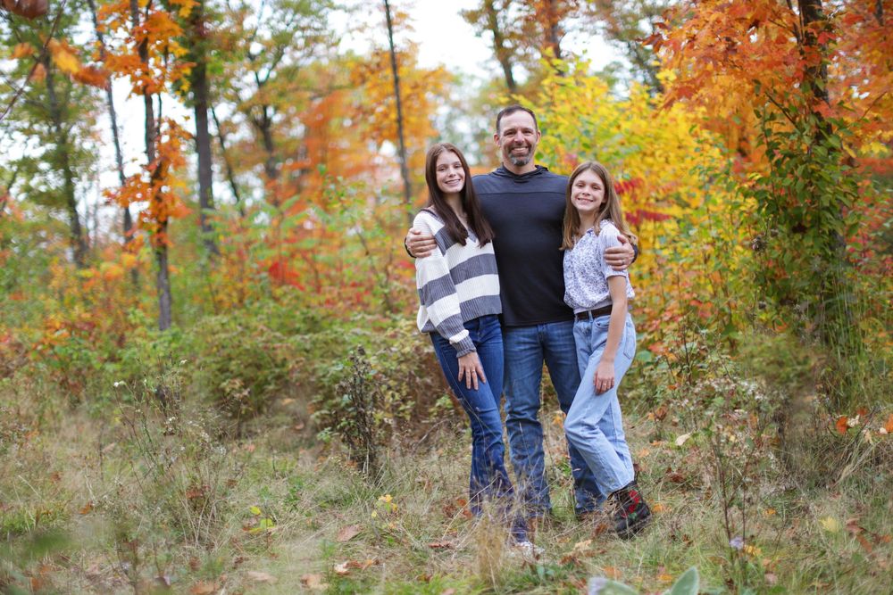 People gather for a casual photo shoot surrounded by beautiful autumn colors in a wooded area.