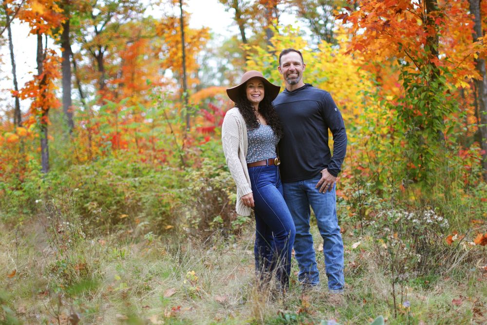 People gather for candid moments in a wooded area with golden fall colors in the background.