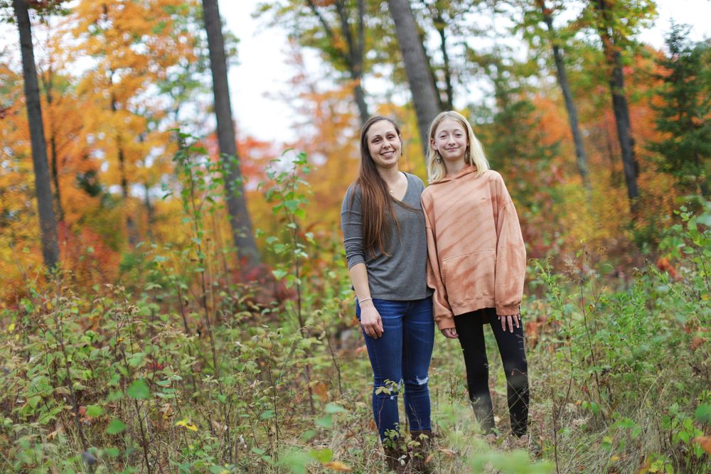 Two people stand together on a forest path surrounded by vibrant autumn foliage and colorful fall trees.