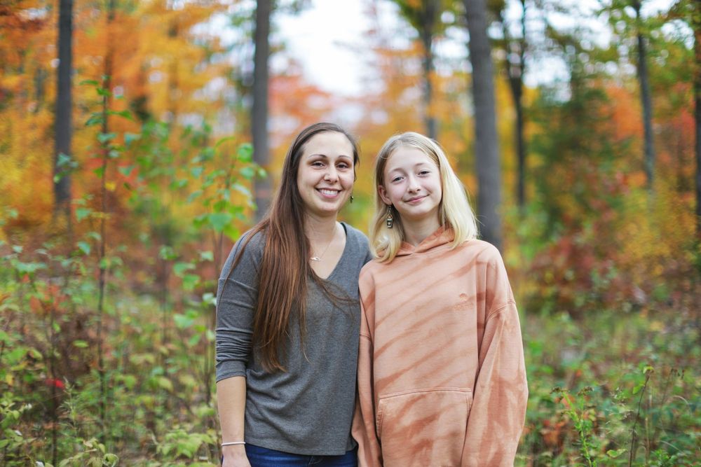 A couple stands together in a vibrant autumn forest with orange and red foliage creating a warm backdrop.