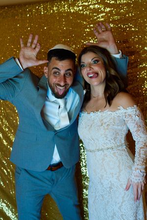 Wedding couple posing playfully against a sparkly gold backdrop.