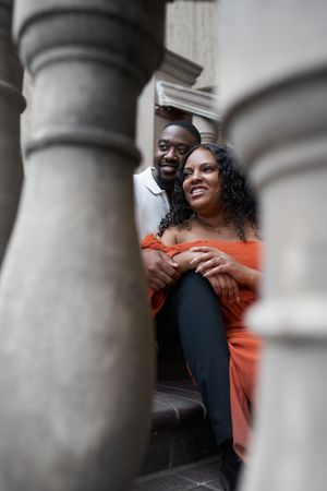 A joyful couple shares a candid moment together while sitting against architectural columns.