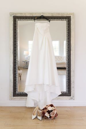 White wedding dress hangs elegantly against a light wall with ornate mirror frame.