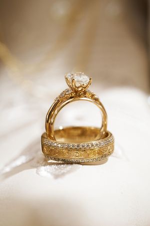 Close-up view of a gold engagement ring with diamond solitaire and intricate band details on white fabric.