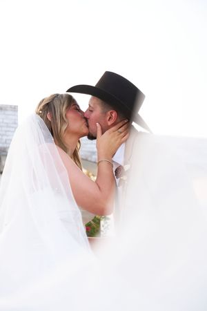 Romantic wedding couple sharing intimate kisses beneath a flowing white veil.