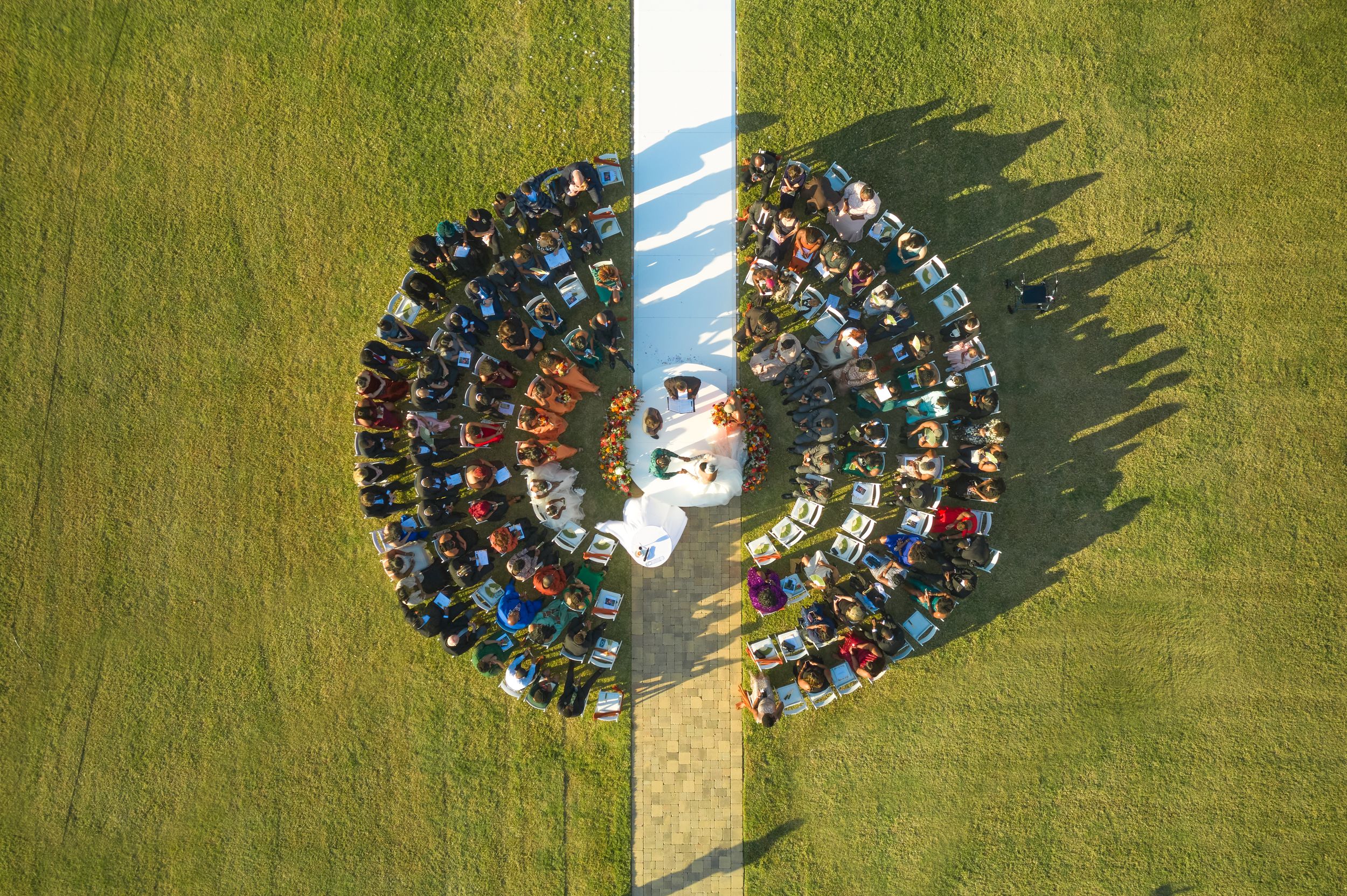 Aerial view of football players forming a circular formation on a green grass field with long shadows.