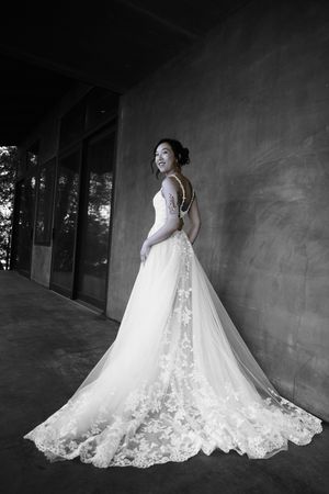 A stunning lace wedding gown with a dramatic train is showcased in an artistic black and white portrait.