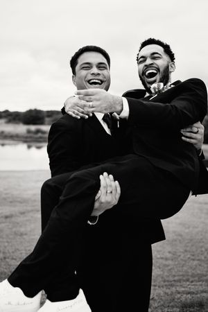Groomsmen in black suits playfully carrying and posing together in a fun outdoor group photo.