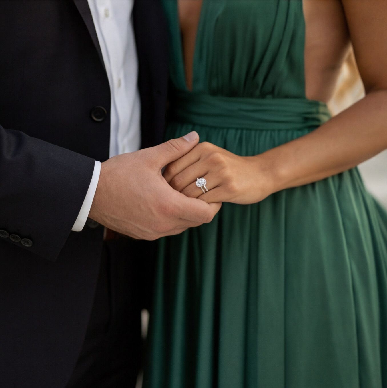 Close-up view of hands exchanging rings during a wedding ceremony, with emerald green dress in background.