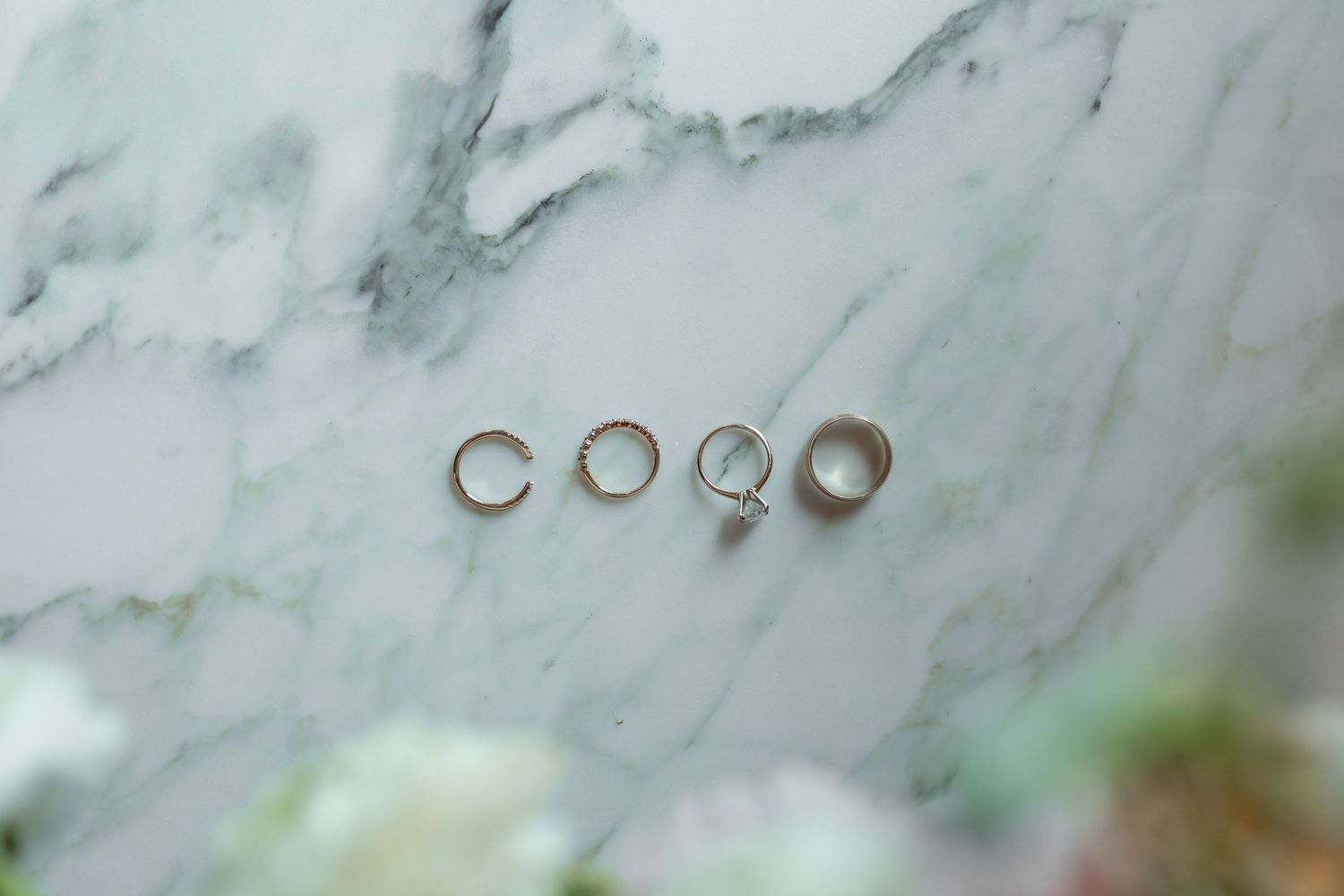 Wedding rings and engagement ring arranged in a row on white marble surface with soft natural lighting.