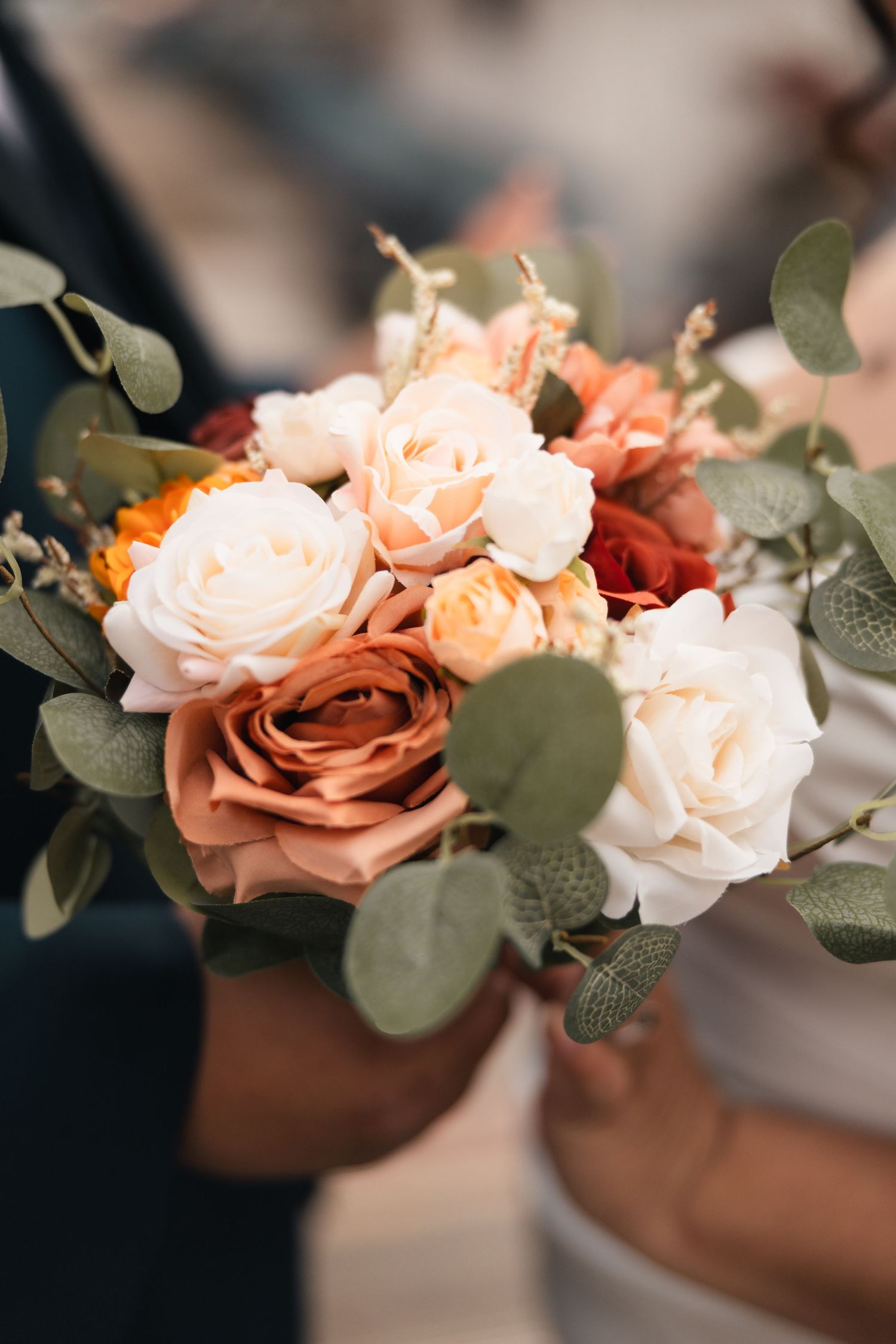 Close-up of peach and cream roses with eucalyptus leaves in a wedding bouquet.