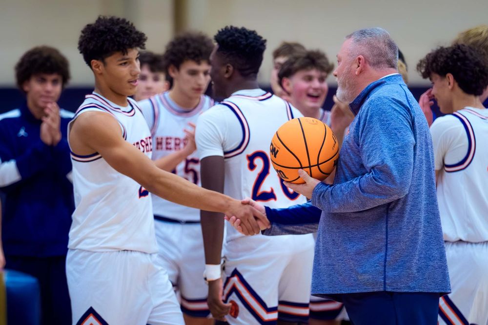 Hershey basketball coach presents Cam Sweeney with the game ball surrounded by teammates after his 1,000th point.