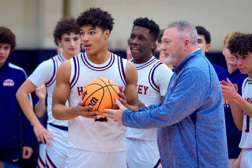 Cam Sweeney is congratulated by his coach while holding the game ball after scoring his 1,000th point for Hershey High School basketball.