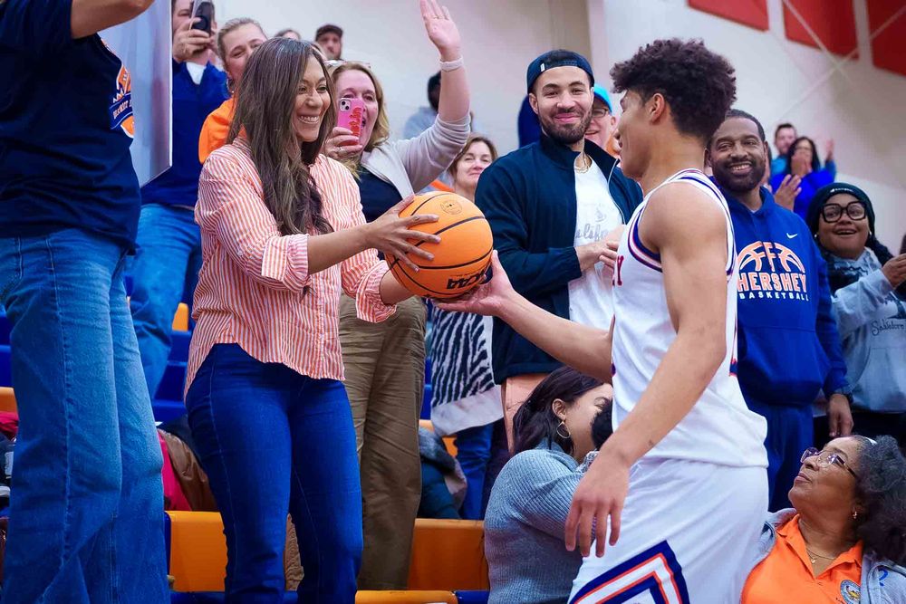 Cam Sweeney holding the basketball and sharing a moment with family and friends in the stands after his 1,000th point.