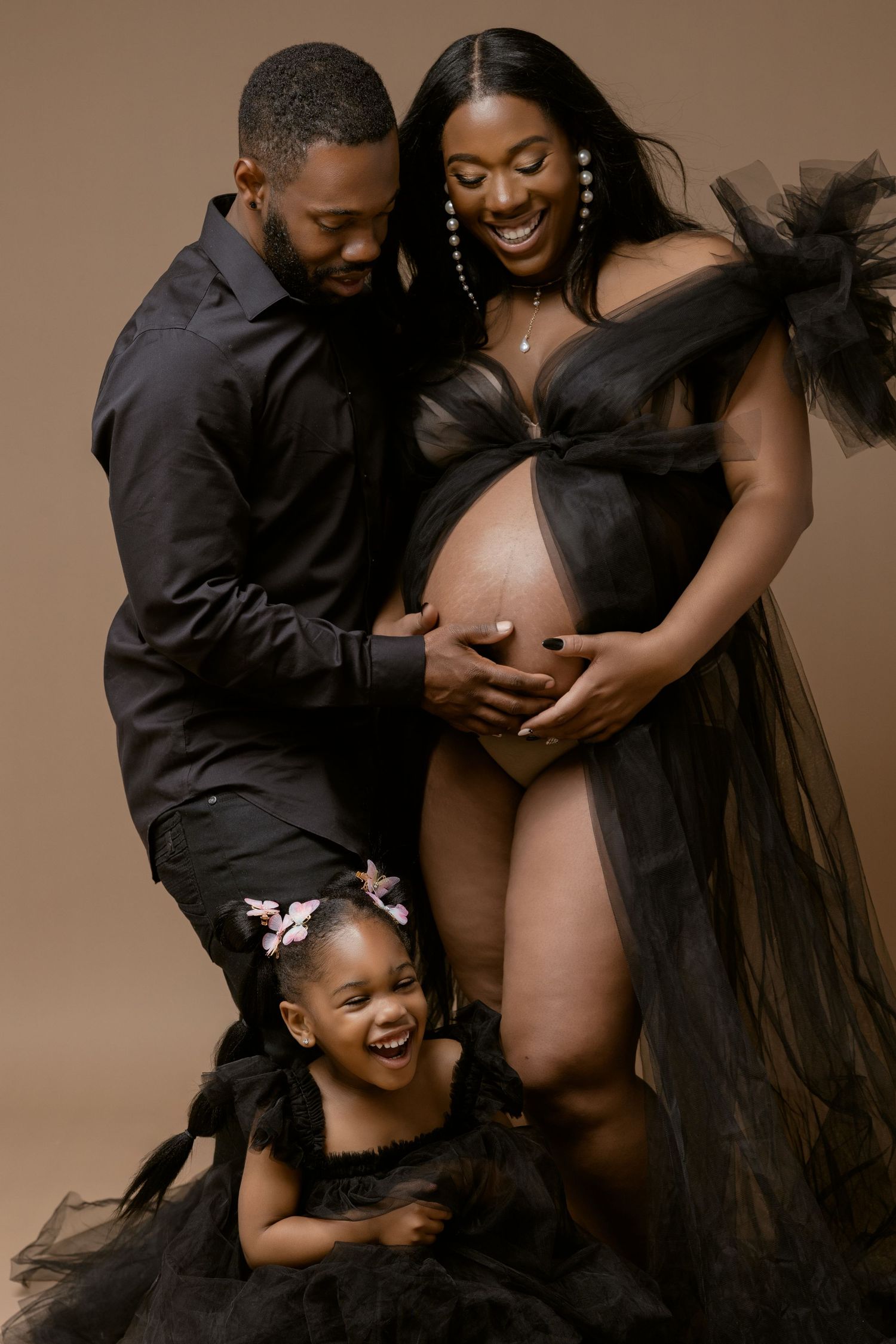 Black and white portrait of a family with a toddler and pregnant woman smiling joyfully together.