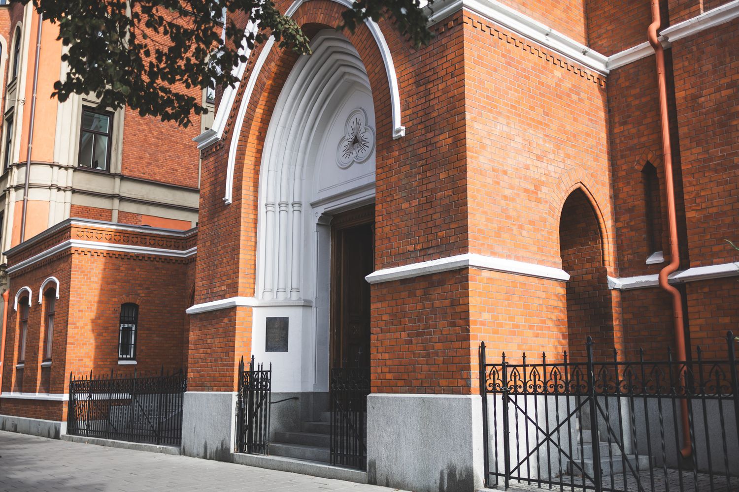 Red brick church exterior with white arched doorways and stone steps leading to multiple entrances.