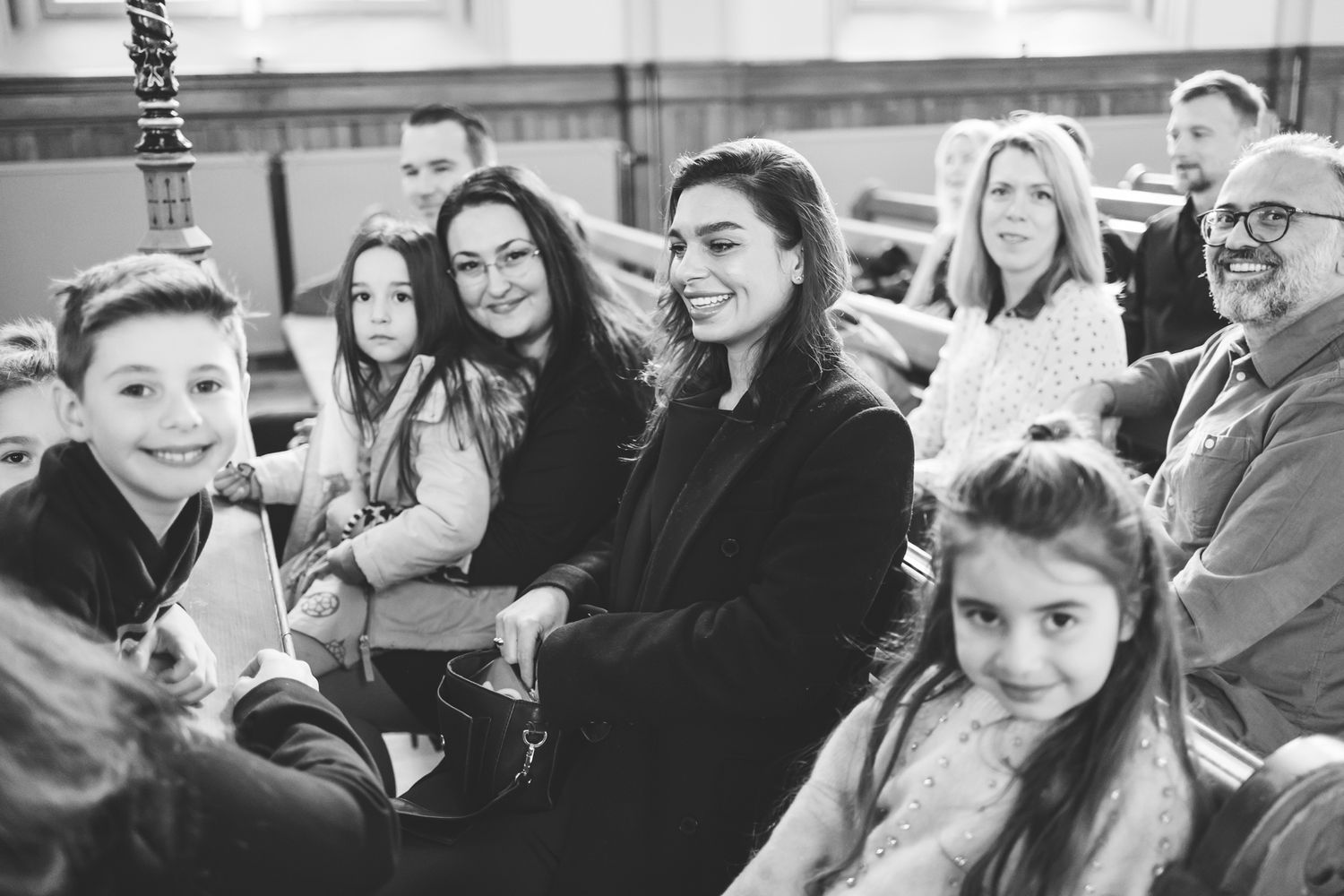 A black and white candid photo shows a group of people sitting together and laughing at an indoor event.