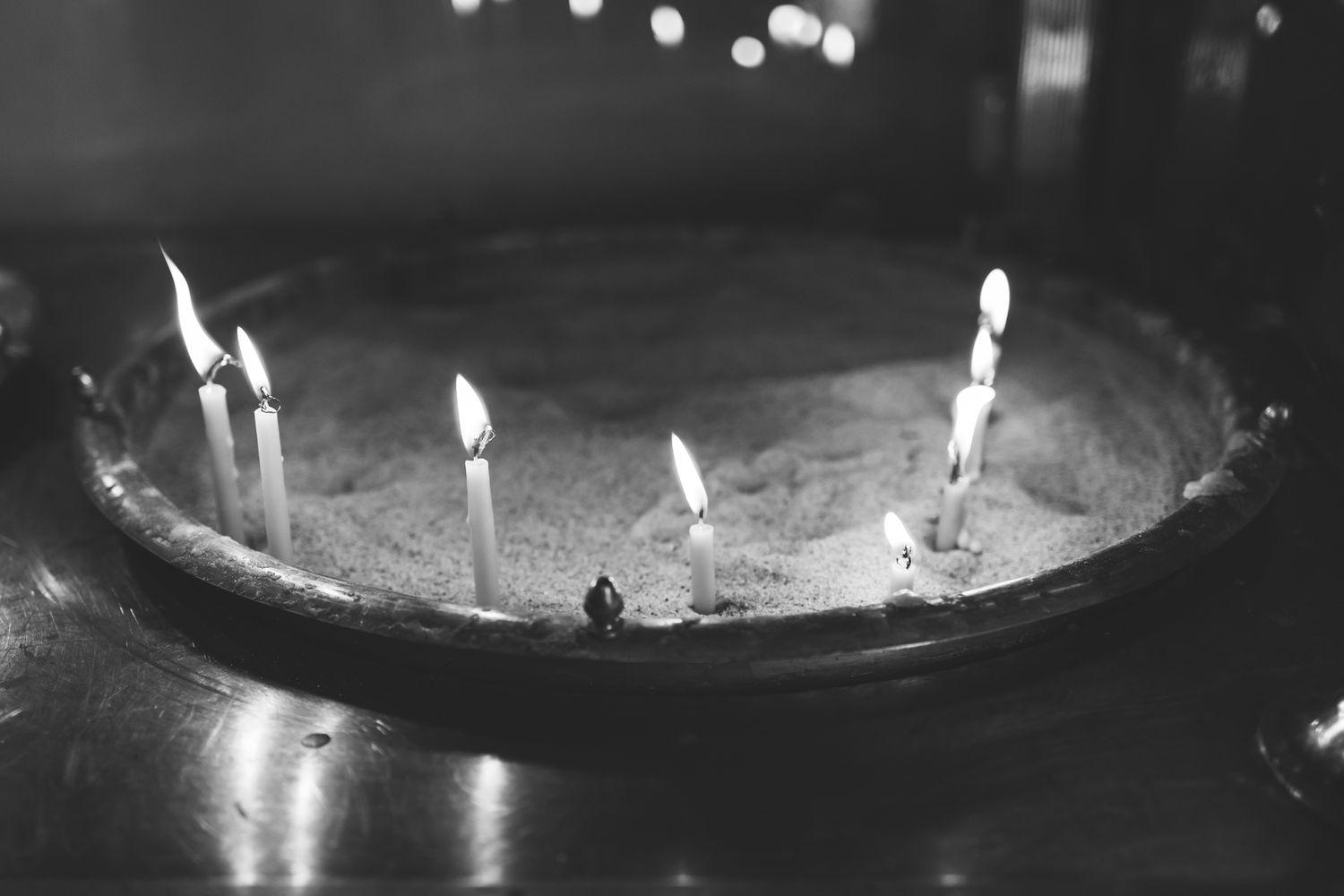 Lit birthday candles glow in black and white on a round cake surface.