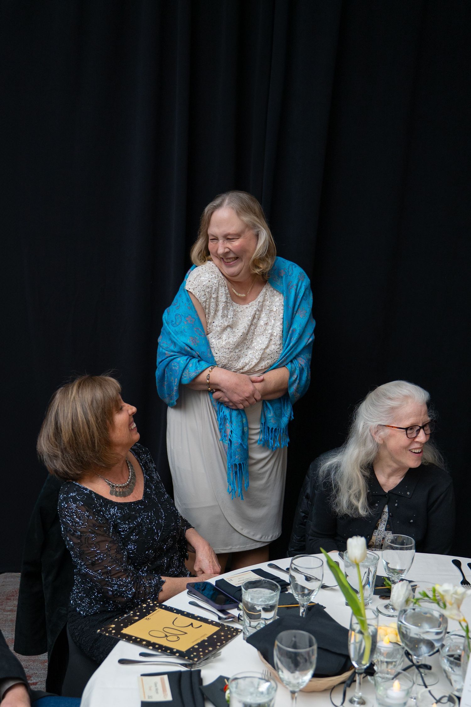 Three women comfortably laugh together at a formal fundraising gala event by Valley House at Canyon Crest Event Center in Twin Falls, Idaho.