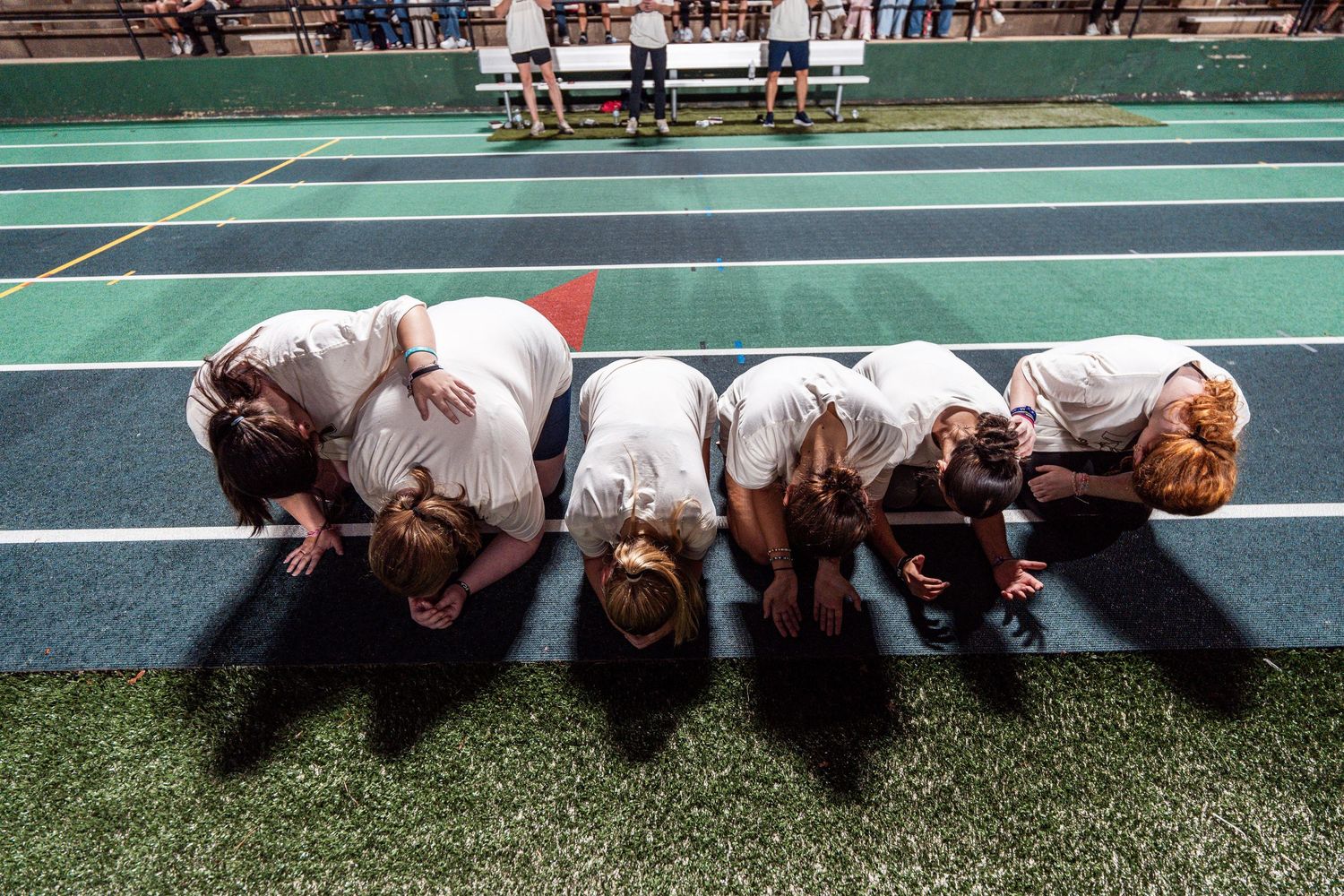 A group of athletes lying face down on a green sports field performing synchronized stretching exercises.