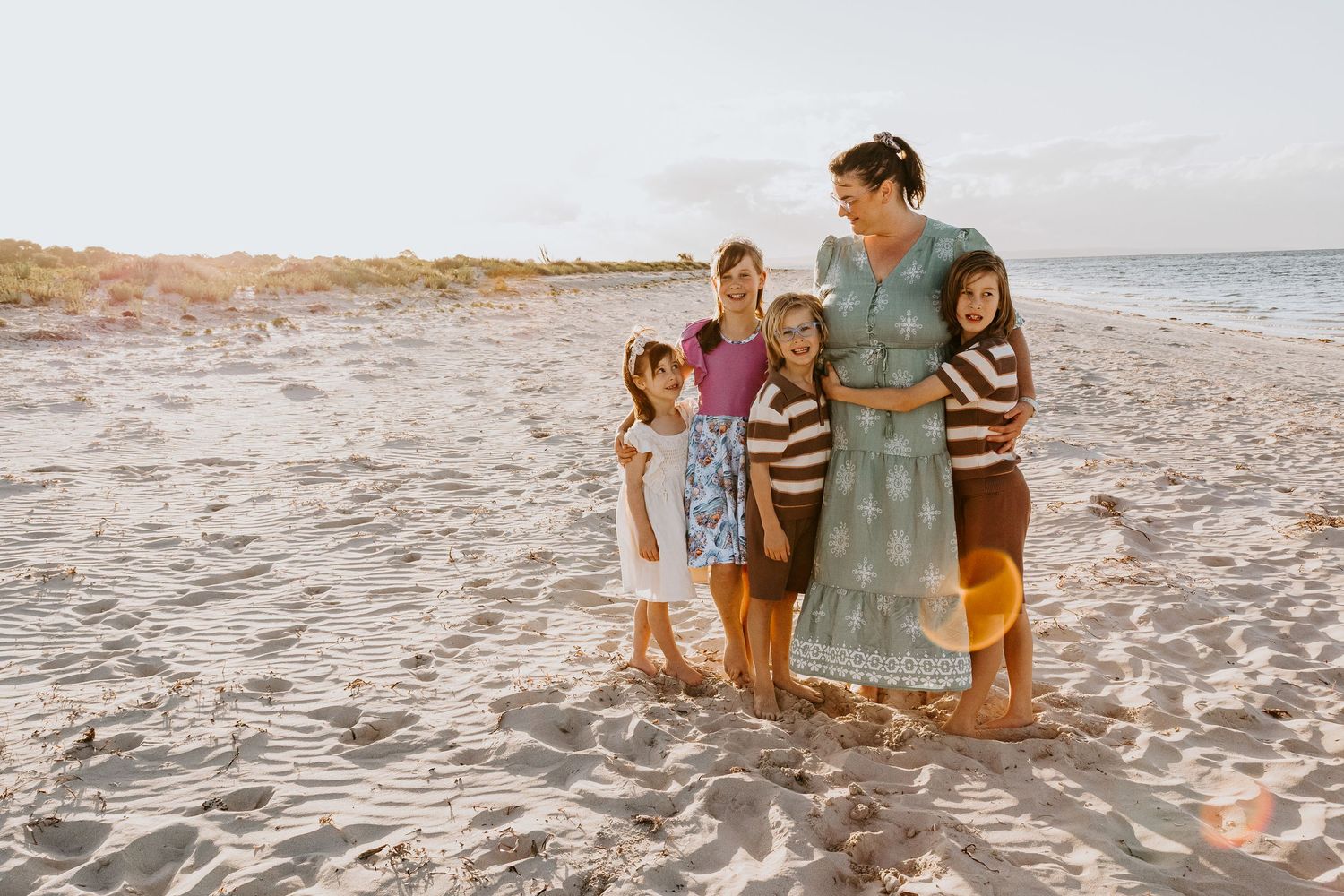 Family walking together along a scenic beach at sunset, creating footprints in the sand.