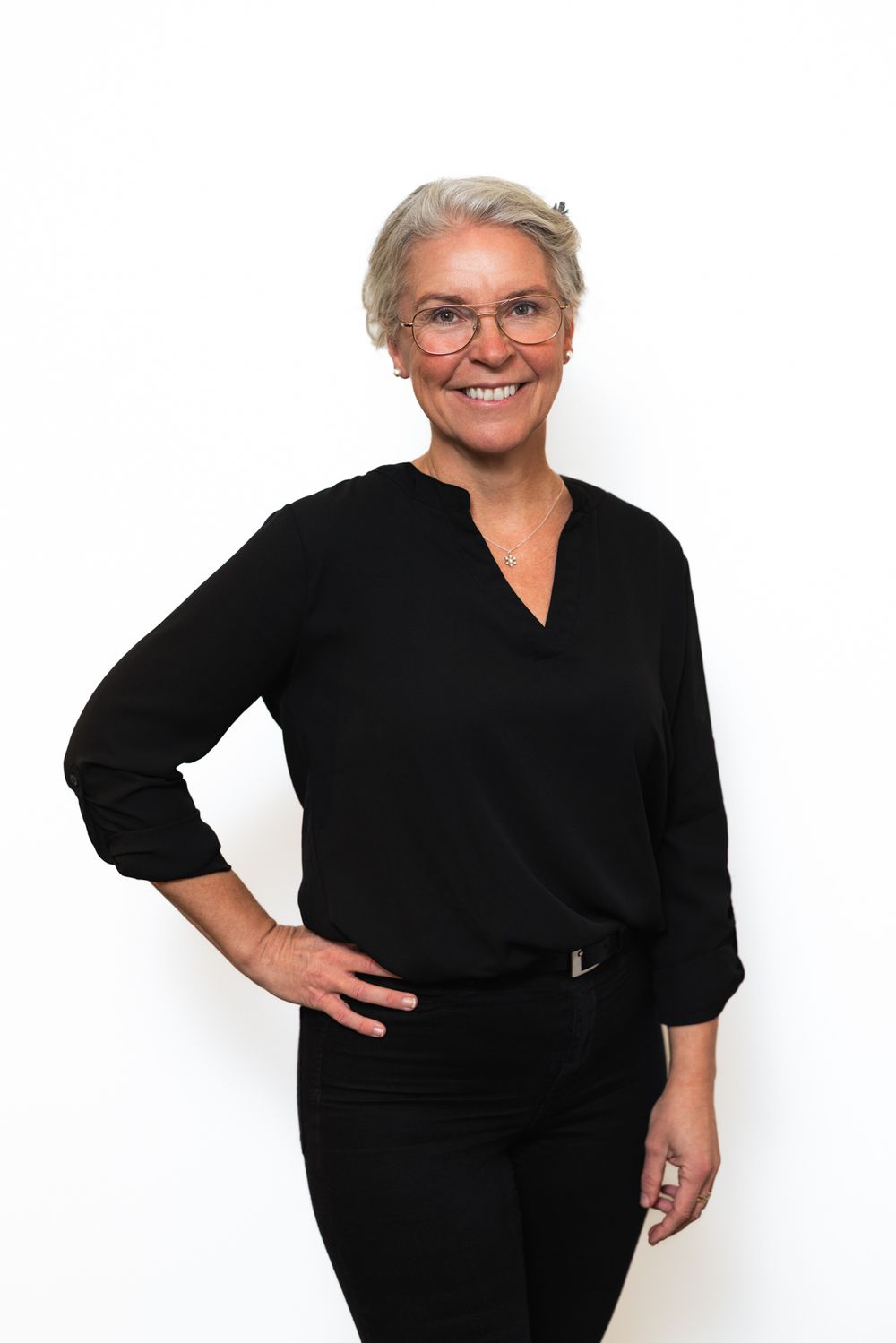 Professional portrait of a person in a black v-neck blouse and glasses smiling against a white background.