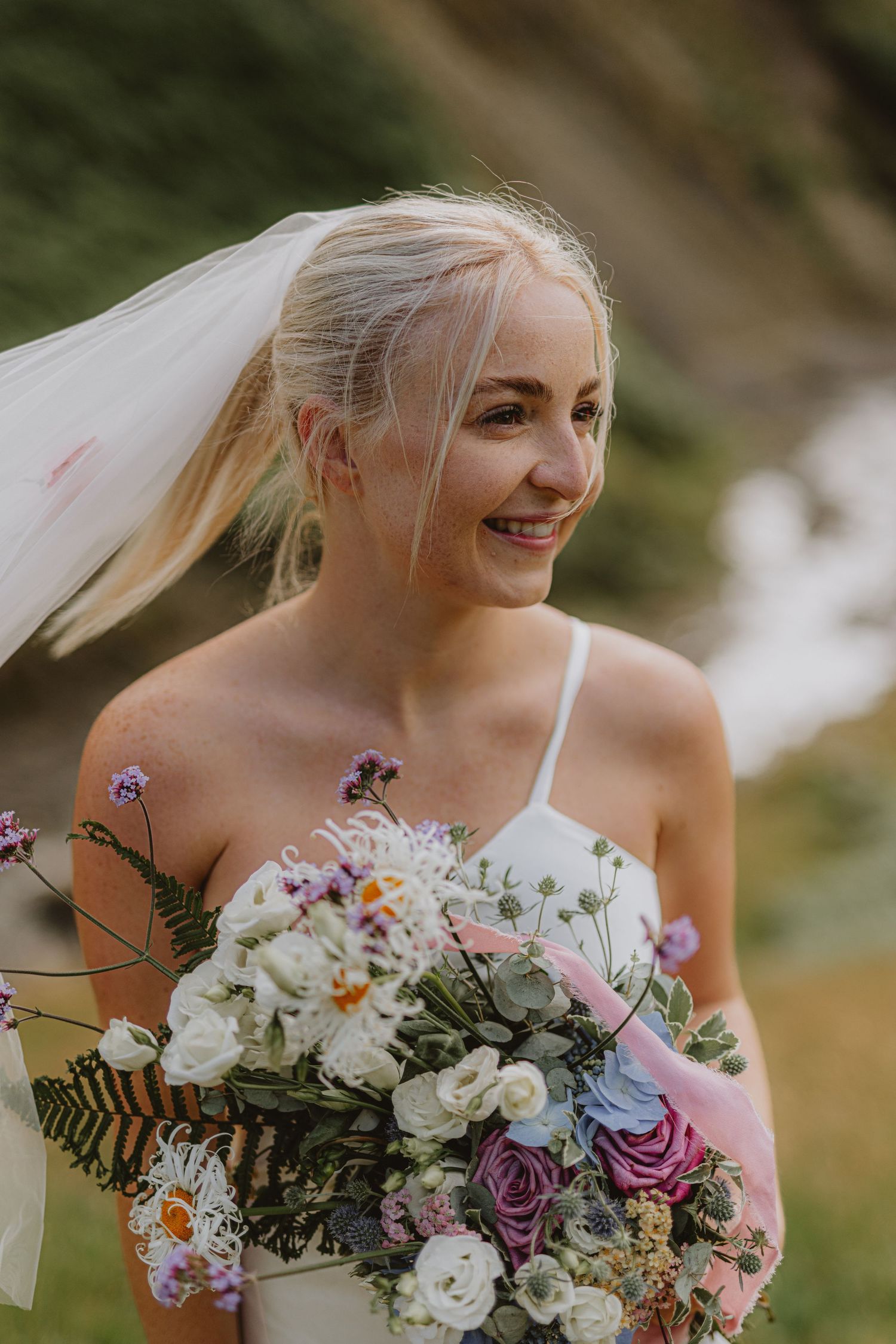 A delicate bridal bouquet with light blue and white flowers mixed with cascading greenery and ferns.