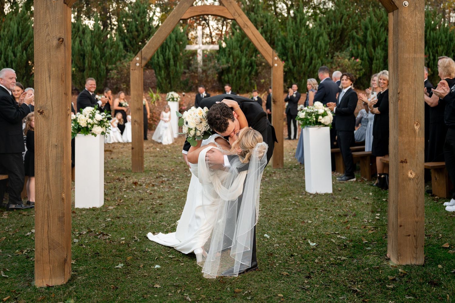 Couple dancing and celebrating at an outdoor wedding reception with wooden posts and string lights.