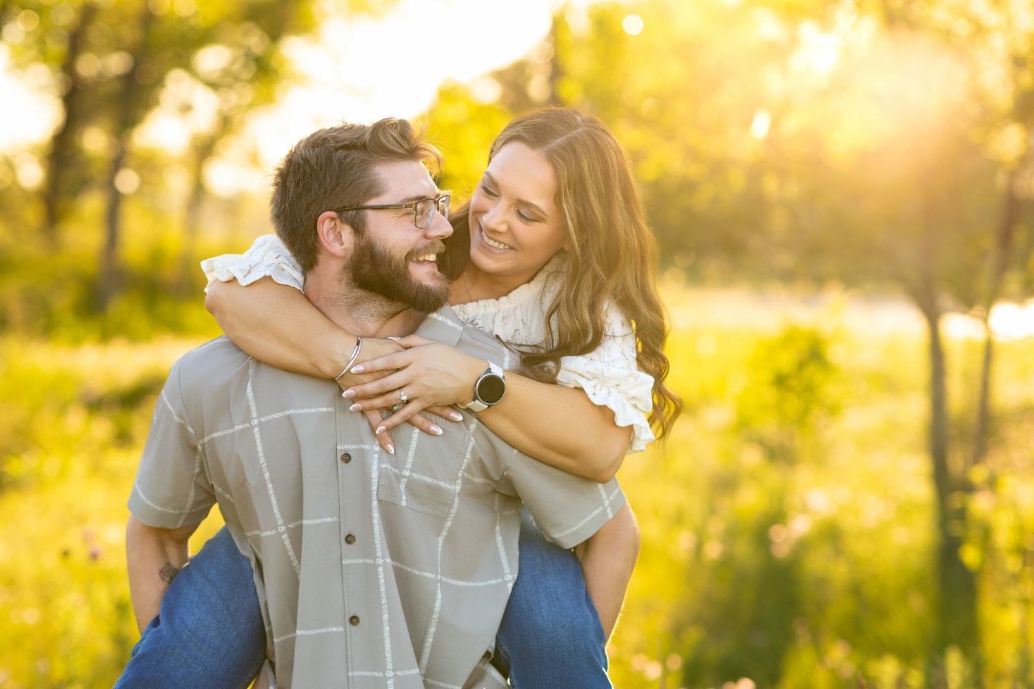 An engagement couple embraces lovingly in a sunlit park during golden hour with warm autumn colors in the background.