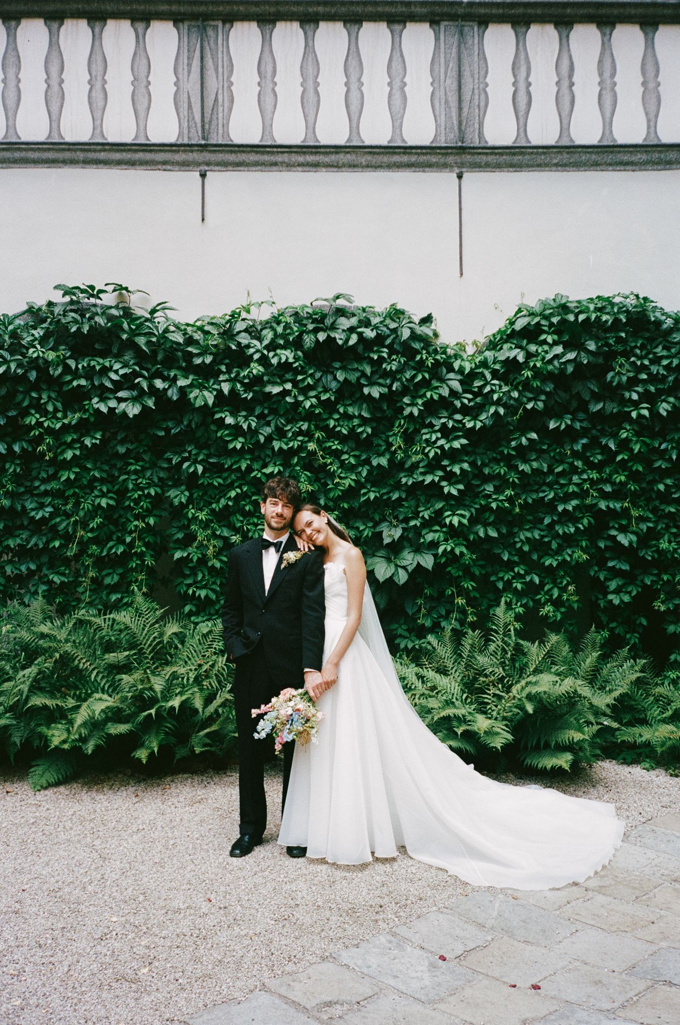 Elegant bride and groom posing before an ivy-covered wall with ferns at their wedding venue.