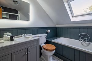 Modern grey bathroom with sloped ceiling, freestanding tub, and wooden paneling.