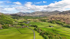 Aerial view of green valley with winding road through pastoral countryside and mountains.