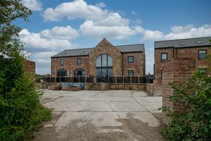 Wide view of brick buildings with parking area and landscaped grounds under puffy clouds.