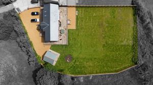 Aerial view of a beige house with a large green lawn and grey surroundings.