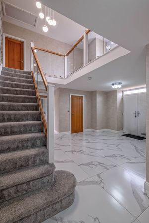 Modern entryway with marble floors, carpeted stairs, and hanging pendant lights in a luxury home.