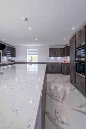 Sleek modern kitchen with marble floors, dark cabinets, and white countertops extending into a long island.