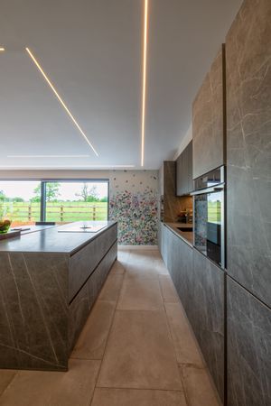 Modern kitchen with dramatic lighting, stone surfaces and floor-to-ceiling windows overlooking countryside.