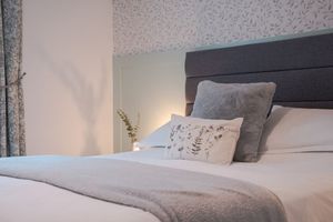 Cozy bedroom with grey and white bedding, decorative pillows and neutral decor.