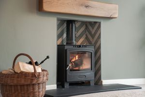 Wood burning stove with herringbone tile backdrop and wooden beam mantel.