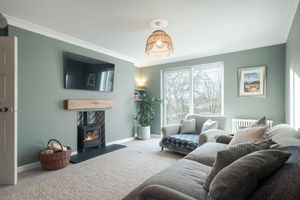 Living room with grey sofas, wall-mounted TV, and wood burning stove in sage green walls.