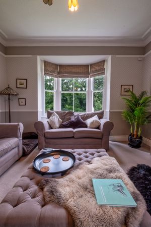 Elegant living room with bay window, plush furniture, and ottoman decorated with sheepskin throw.