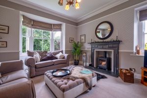 Traditional living room featuring bay windows, ornate fireplace, and comfortable brown sofas.