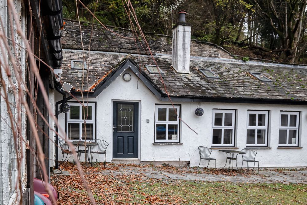 Charming white cottage with stone walls and blue door nestled against a hillside.