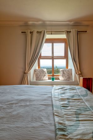 Panoramic view of unmade bed with window overlooking countryside landscape.